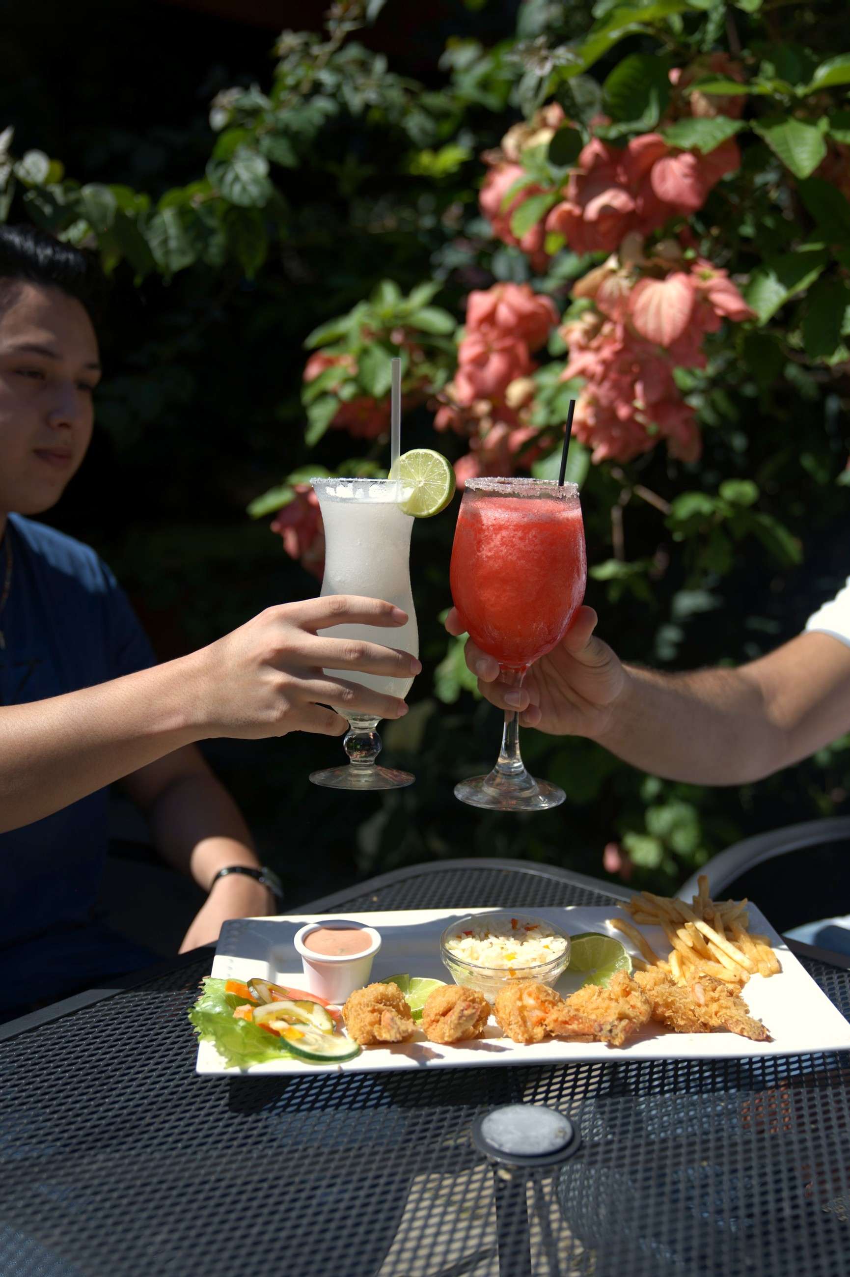 Two people toasting with cocktails in front of flowers