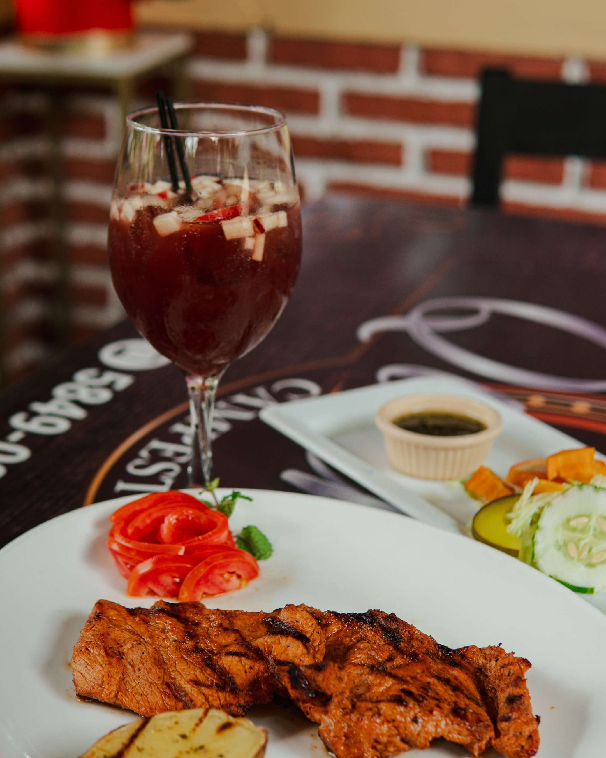 Copa de sangría con fruta junto a un plato a la parrilla