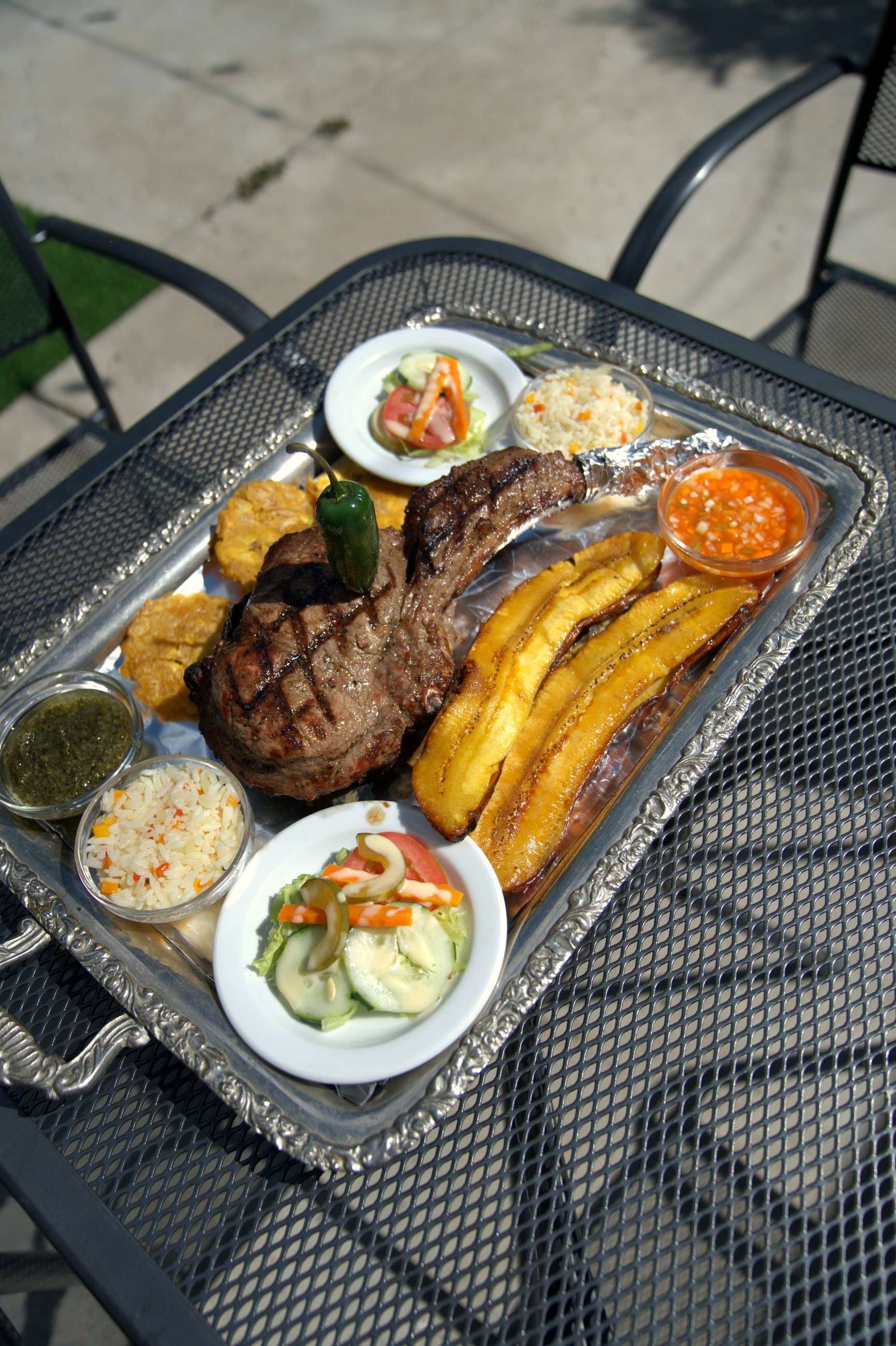 Bone-in steak on a silver tray with fried plantains