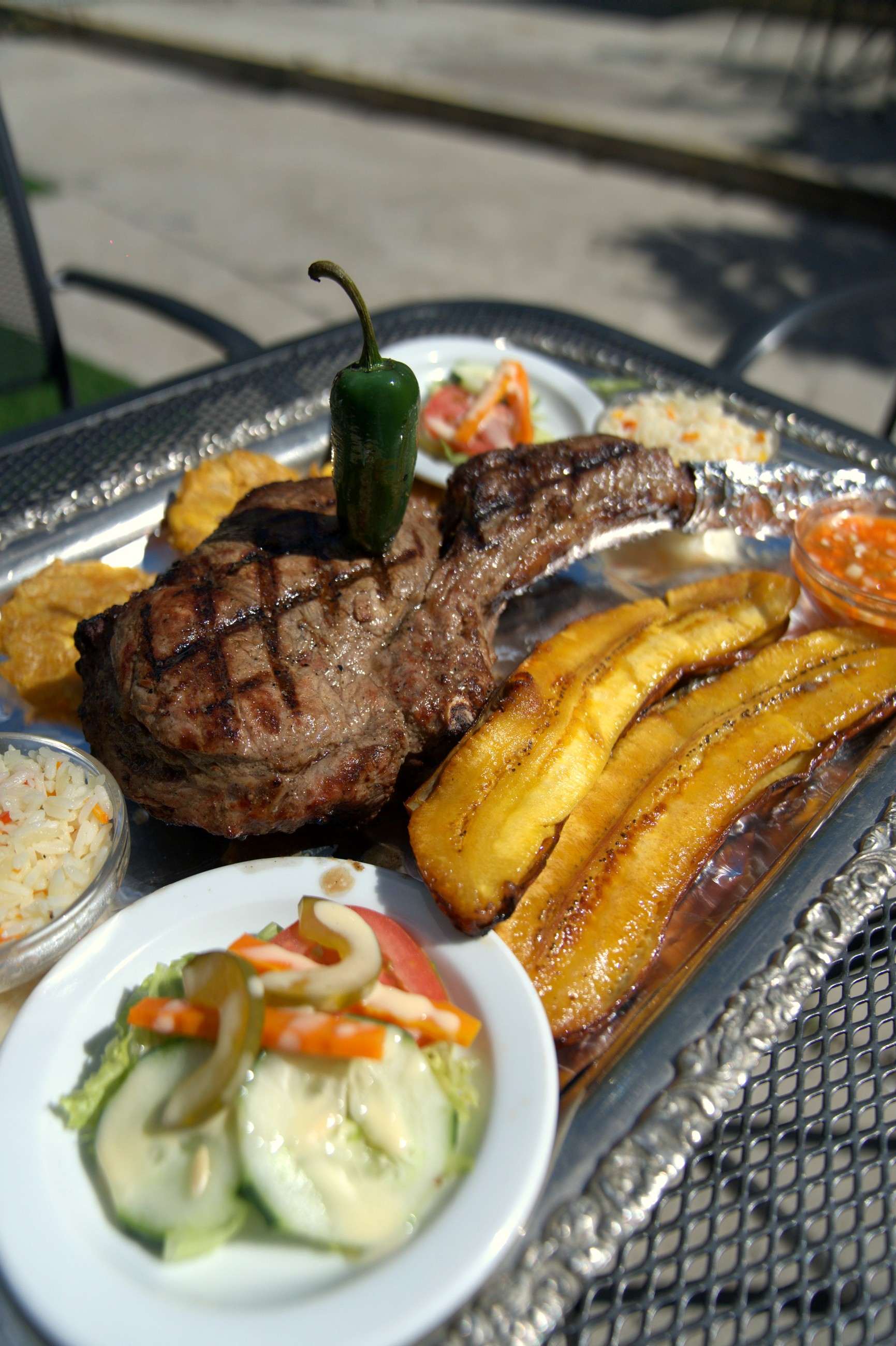 Bone-in grilled steak with fried plantains, rice and salad